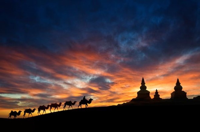 Contrasting image of a temple and a line of camels against a setting sky